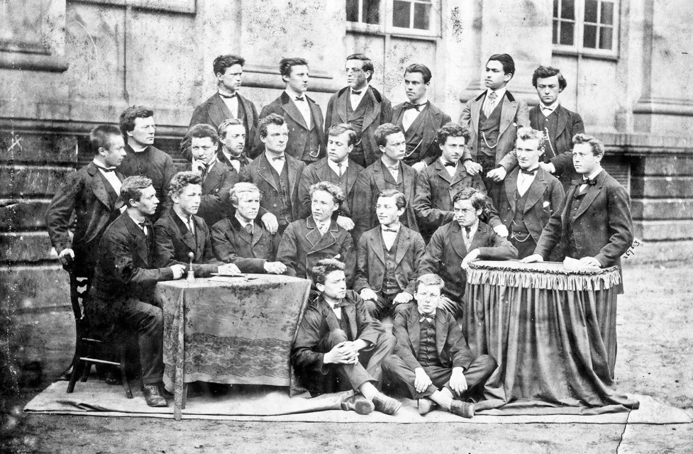 De Lettergilde van het Klein Seminarie van Roeselare (1874-1875) met Jules Devos (bovenste rij, uiterst rechts), Hugo Verriest (derde rij, uiterst links) en naast Verriest Albrecht Rodenbach. De poësisklas kwam tijdens het superiorfeest van 1875 in botsing met superior Henri Delbar, wat leidde tot de uitsluiting van Devos. Het conflict ging onder de naam De Groote Stooringe de geschiedenis in. (Collectie Stad Antwerpen, Letterenhuis, tglhph3046)