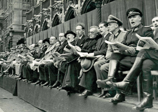 Achtste Vlaams Nationaal Zangfeest in Brussel, 31 augustus 1941. Zicht op de eretribune op de Grote Markt, met o.a. secretaris-generaal Victor Leemans (8ste van rechts), Hendrik Elias (7de van rechts), August Borms (6de van rechts), Cyriel Verschaeve (4de van rechts) en Jef van de Wiele (3de van rechts). (ADVN, VFAL122)