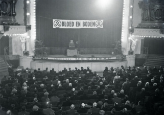 Een meeting van Volksverwering in Antwerpen, 15 december 1940. Op de achtergrond het logo van de organisatie met haar devies 'Bloed en Bodem'. (Kazerne Dossin)